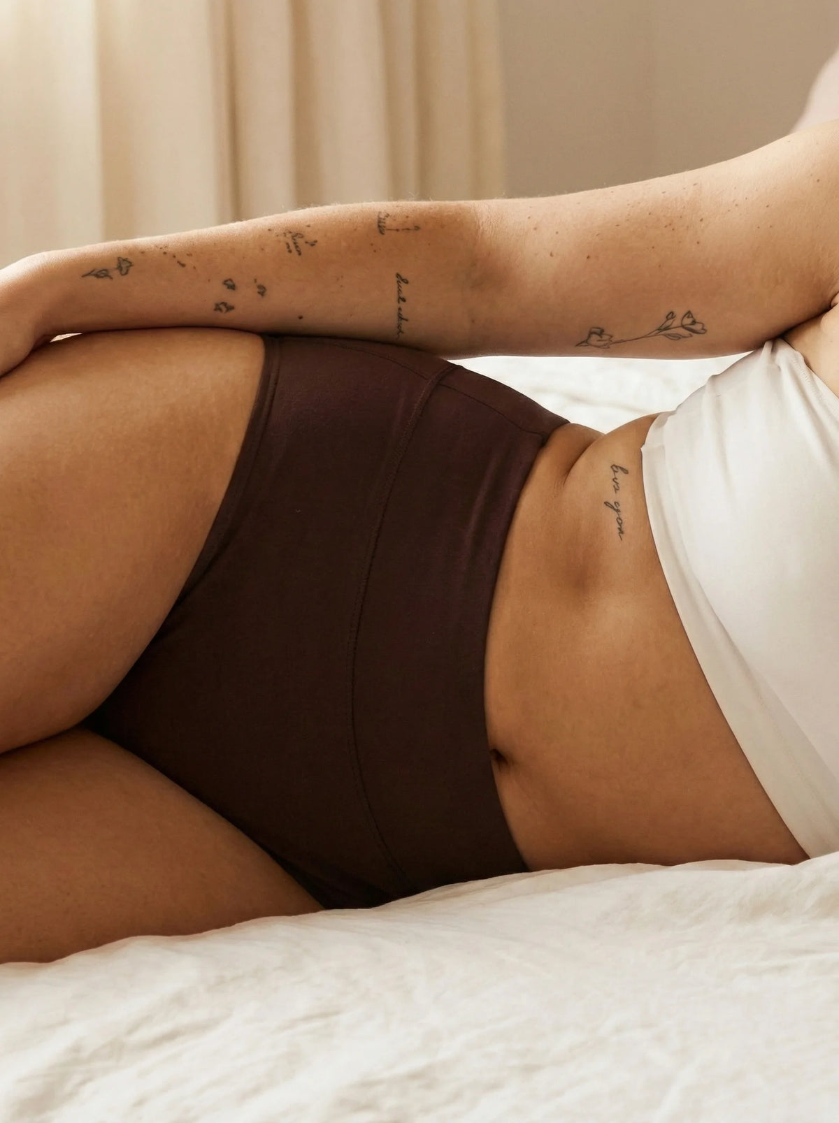 Menstruatie ondergoed donker bruin, close-up van gedragen huggster brief in een lifestylebeeld op bed